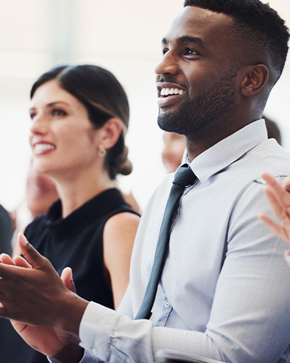 Two young professionals in a crowd clapping for a presentation